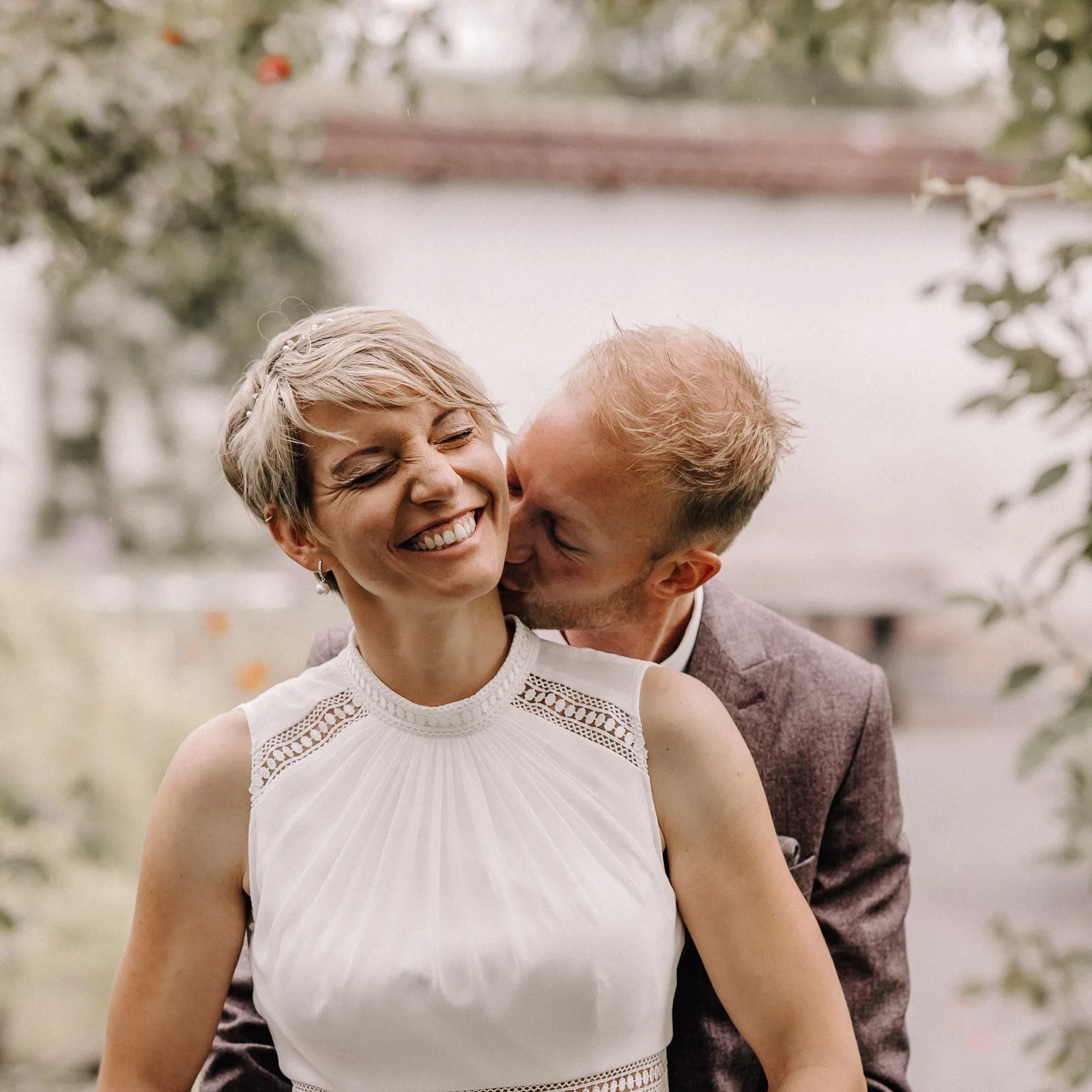 Hochzeitsfotograf Schweiz- Bräutigam küsst Braut am Hals Braut lacht-Boho style