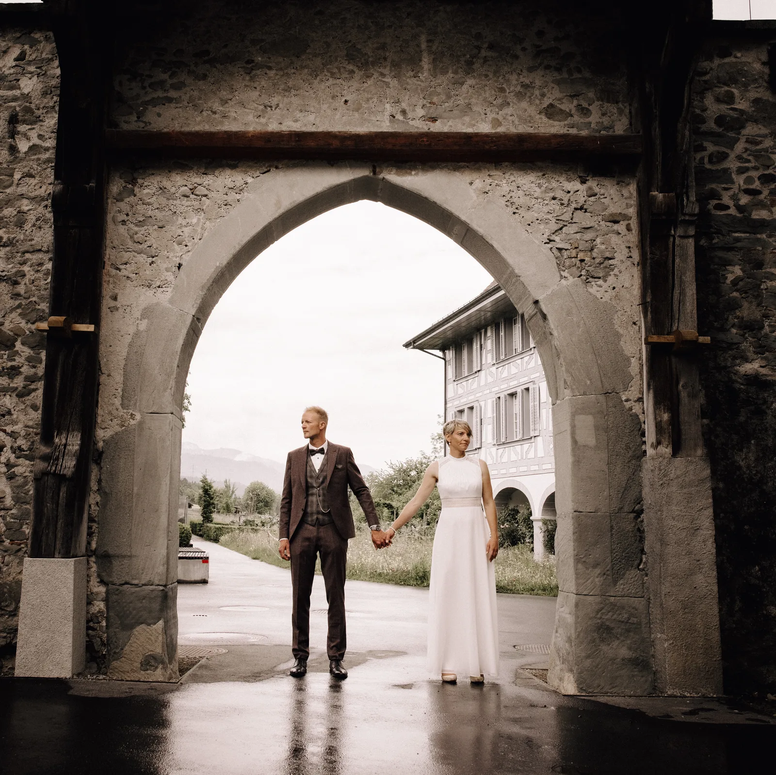 Hochzeitsfotograf Luzern-Brautpaar steht händehaltend unter Torbogen